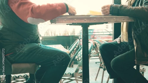 Two unrecognizable senior men talking while seated at a cafe table near a window