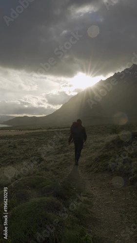 Silhouette of a hiker walking on a trail toward a lake during sunset in nature