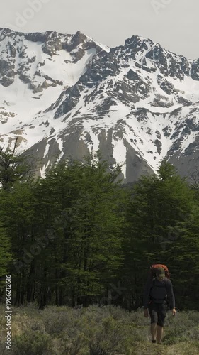 Hiker walking in front of a forest and snow-covered mountains in nature