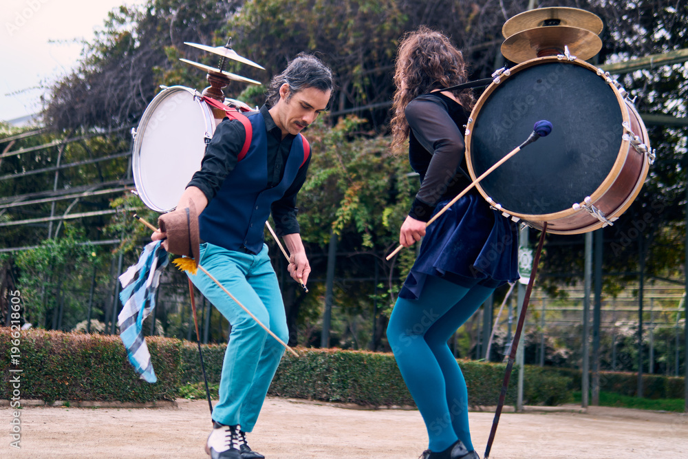 Obraz premium Adult couple of urban dancers, happily playing and dancing the cueca with a bass drum on their backs outdoors, Chilean chinchineros, street musicians who play the bass drum and dance in the streets.