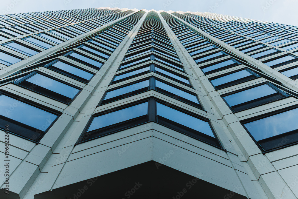Obraz premium View of a tall building from the ground looking up at the windows and sky showing the angle of the architecture against the blue background