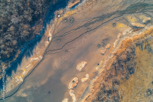 Dried riverbed at forest edge with cracked earth and mud, environmental drought and climate change impact, aerial drone shot from above