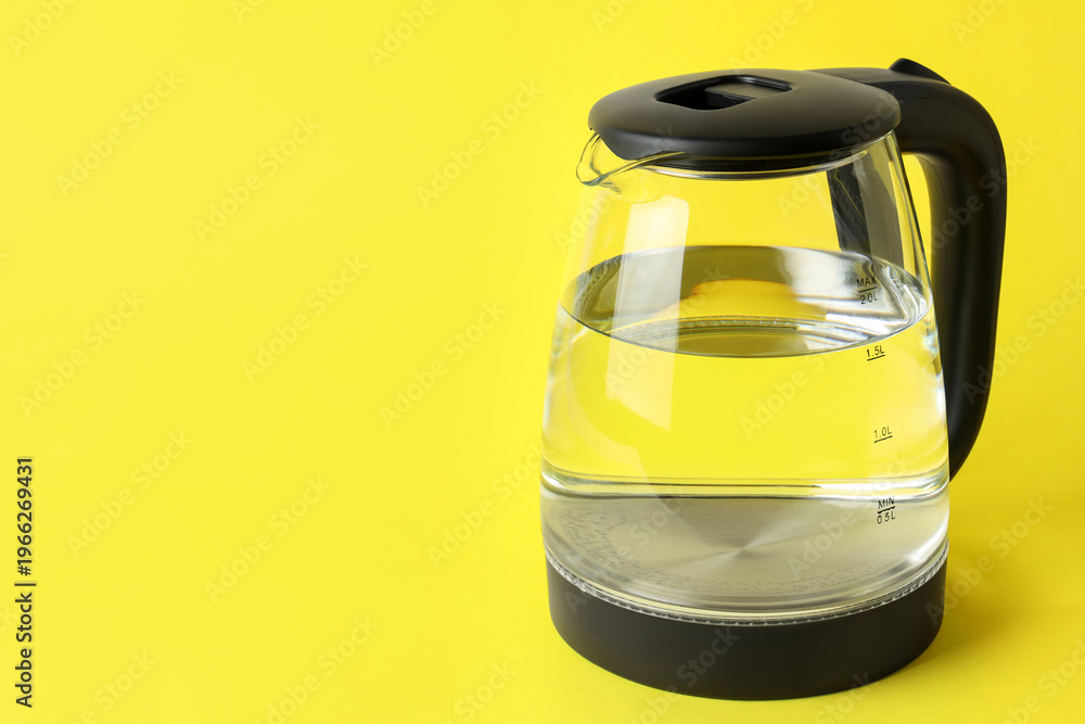 Fototapeta premium Modern electric kettle with water on yellow background. Space for text