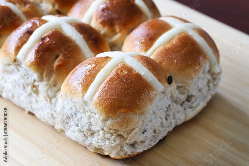 A close up shot of some freshly made hot cross buns on the wooden cutting board.