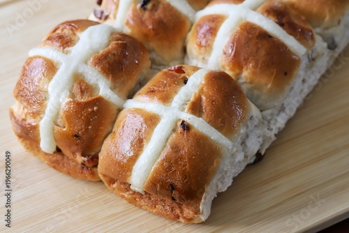 A close up shot of some freshly made hot cross buns on the wooden cutting board.