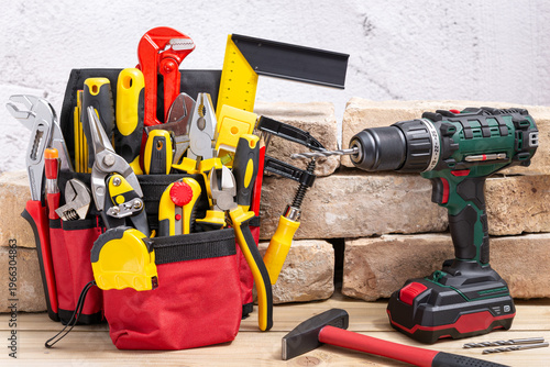 Tool belt with tools and screwdriver drill next to old bricks
