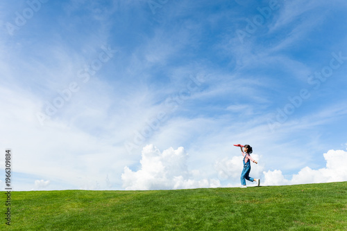 A little girl playing with a toy airplane under a blue sky with white clouds