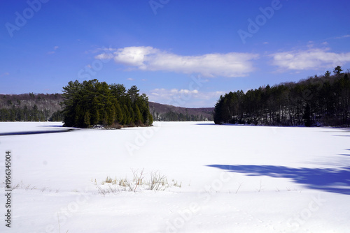 A vast, snow-covered expanse of frozen Lac Philippe is framed by densely forested hills under a vibrant blue sky in Gatineau Park, Quebec
