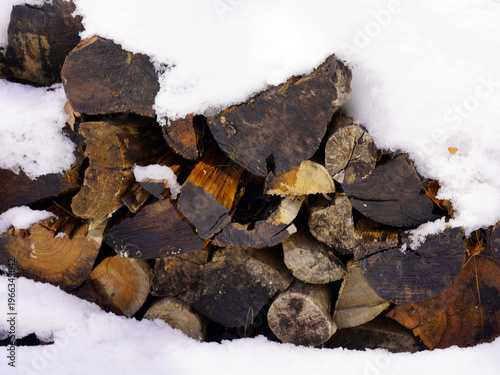 A neatly stacked pile of cut firewood sits partially covered by a thick layer of fresh white snow in Gatineau Park, Quebec