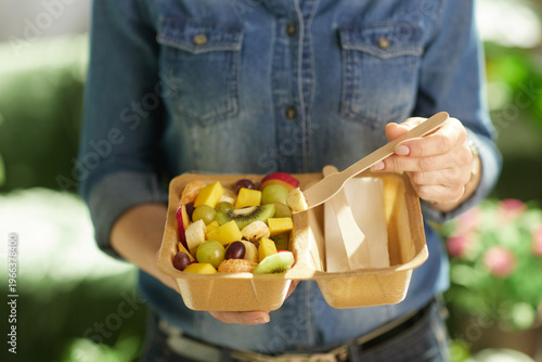 A detailed shot of a woman holding a variety of cut fruits in a fiber-based container, illustrating healthy snacking and sustainable food choices.
