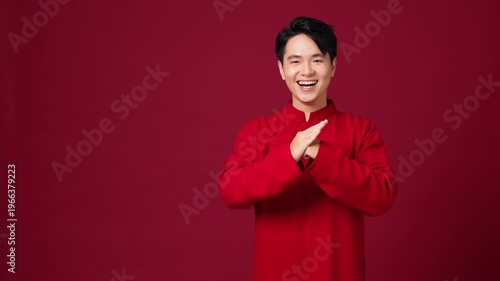 Asian man greeting with clasped hands, saying New Year's greetings in Chinese. Red festive outfit, classic Lunar New Year pose. Copy space