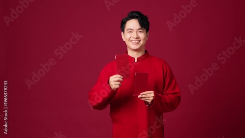 Asian man with traditional outfit, holding red envelope, smiling confidently, traditional New Year greeting.