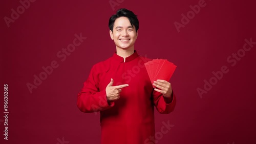 Asian man pointing while holding red envelope, confident and cheerful New Year pose. Copy space