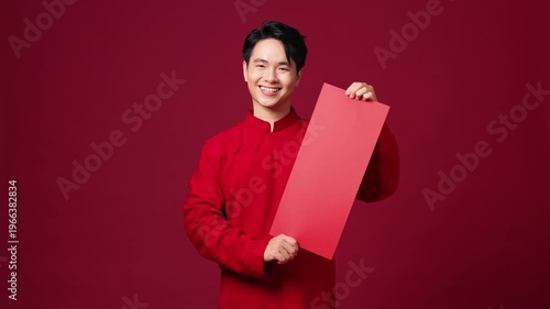 Asian man holding vertical blank red banner, smiling, clean background for holiday messaging. Space for design