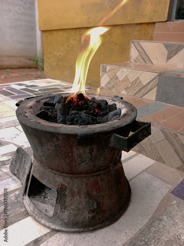 Close up of hot burning black pieces of charcoal with orange flame in coal pot. Fire setup for local or traditional method of cooking, grilling in Africa in olden days or time.