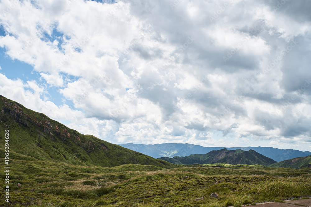 Fototapeta premium Vast volcanic landscape with green mountains, crater terrain and dramatic summer clouds
