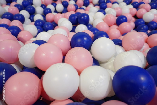 A closeup view of a colorful ball pit filled with many pink, white, and blue plastic balls