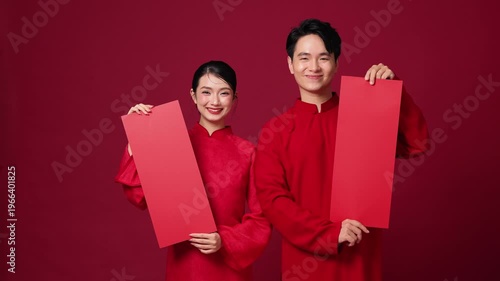 Asian couple holding vertical blank red banners, festive pose, ideal for holiday promotion design