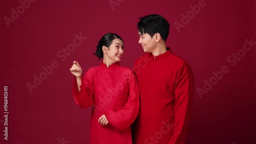 Asian couple standing side by side, smiling softly, red background, calm New Year mood.