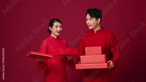 The Asian couple presented a red gift box, their expressions joyful and surprised by the items that flew out, showcasing the idea of giving a holiday gift