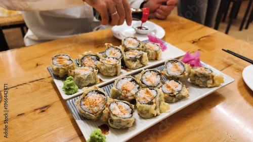 Traditional Japanese Dinner features large platter of baked and hot rolls with ginger and wasabi on wooden table. Cafe setting shows Traditional Japanese Dinner with variety of fusion sushi.