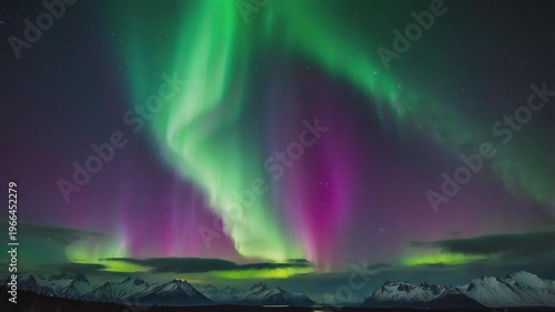 A stunning view of the Aurora Borealis (Northern Lights) over the snowy mountains. The lights dance in a contrasting mix of bright green and magenta.