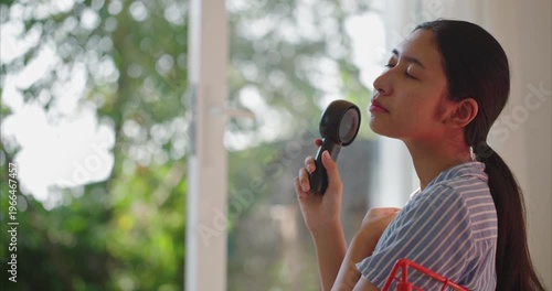 young Asian woman trying to cool herself down with a handheld portable electric fan inside her home during a hot summer day. global warming impact