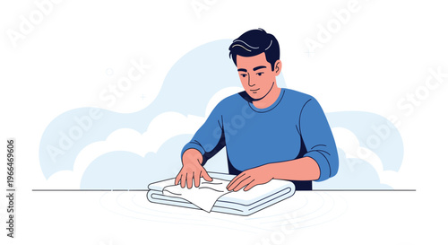 Young man in a blue sweater carefully folding a clean white towel on a table with a soft cloud background behind him.