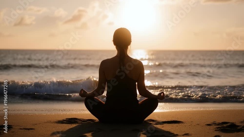Silhouette of woman meditating in lotus pose on beach at sunrise with warm golden light.