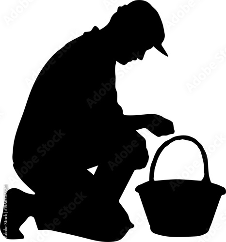 Black Silhouette of a Man in a Cap Crouching Beside a Harvest Basket