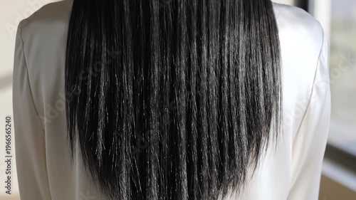 Close-up view of a person's long, straight, dark hair cascading down their back, highlighting its healthy shine and texture