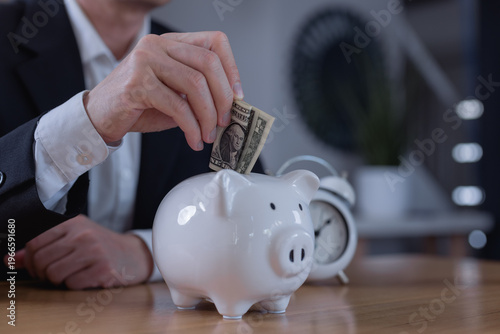 Photos Businessman putting dollar bill into piggy bank, symbolizing saving money, financial planning, investment strategy, personal finance management wealth growth concept for future security