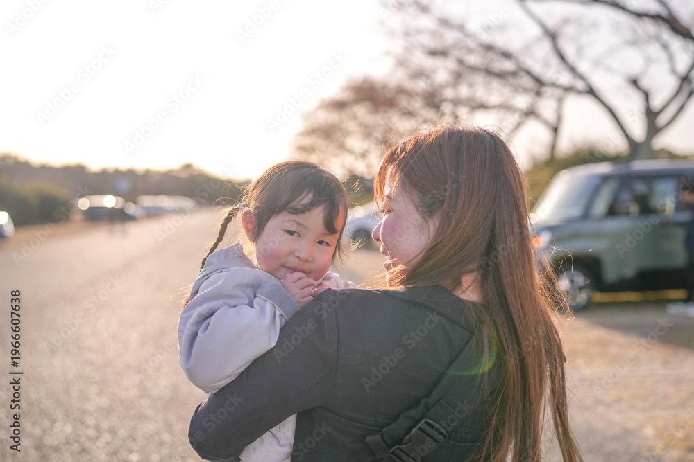 Fototapeta premium Warm sunlight bathes a tender embrace between mother and child. Child smiles softly, eyes bright with delight and affection. Mother's face glows with gentle joy, arms cradling the small one