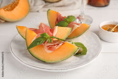 Foto Plate of fresh melon pieces with delicious prosciutto and basil leaves on white