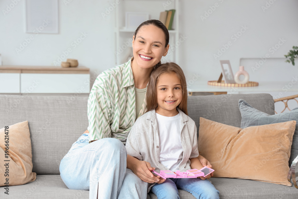 Fototapeta premium Happy young woman and her daughter with cosmetics for kids on sofa in living room