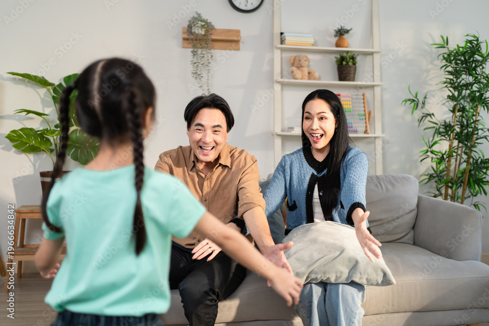 Fototapeta premium Asian girl hugging father and mother on sofa in cozy living room at home. 