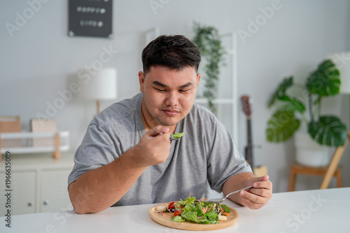 Asian young plus-size man enjoy eating favorite healthy salad in house.