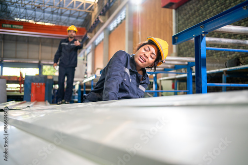 Injured female factory worker in hard hat sitting on floor holding painful leg after accident in steel plant, Concept of workplace occupational hazard, safety risk, emergency and worker compensation