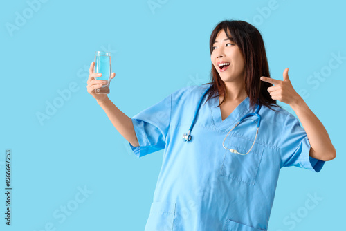 Female Asian doctor pointing at glass of water on blue background
