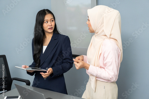 Two diverse asian businesswomen in hijab and suit having serious discussion over laptop in office, Corporate teamwork, professional communication and workplace diversity business management concept