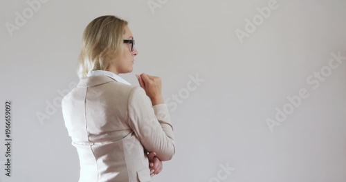 A modern beautiful young woman Caucasian in glasses and a business suit stands on a light background and gestures touchscreen