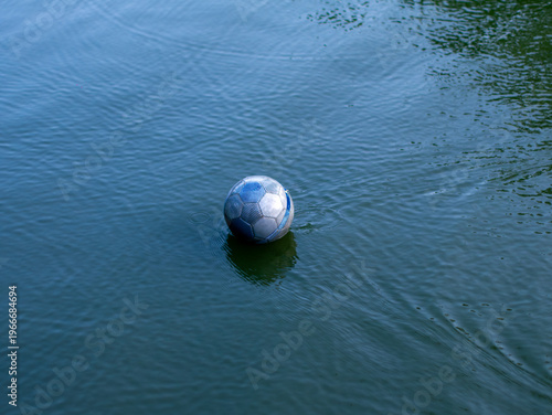 Canvas Print Lone deflated blue and white soccer ball floating adrift on calm dark green lake