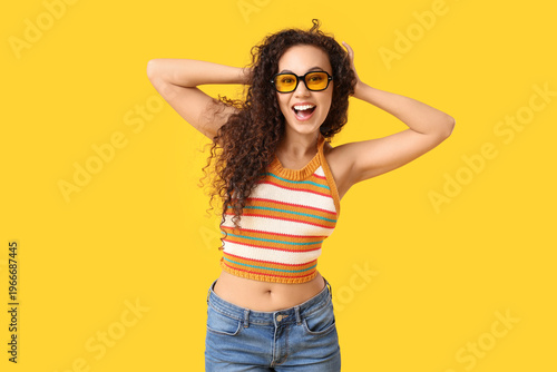 Beautiful African-American woman with sunglasses on yellow background