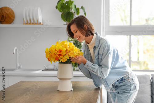 Young woman with daffodils on table in kitchen