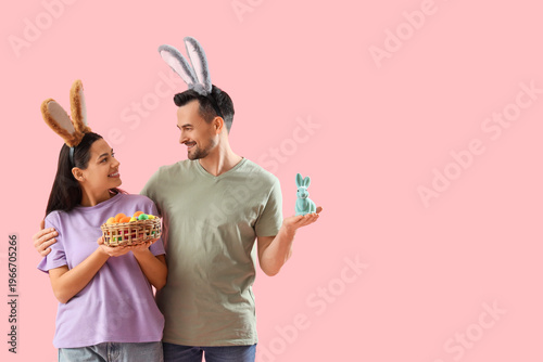 Happy couple in bunny ears with Easter rabbit and eggs on pink background