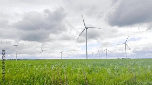 Foreground grassland opening onto a distant line of operating turbines, creating depth between natural terrain and energy structures beneath an overcast rural sky