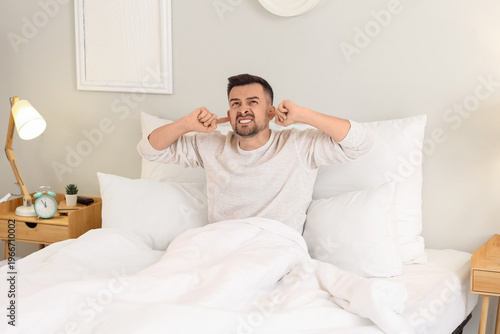 Foto Young man suffering from loud neighbours in bedroom