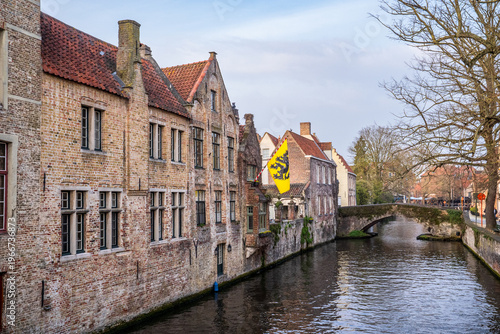 Historic brick houses and canal in Bruges with Flanders flag.