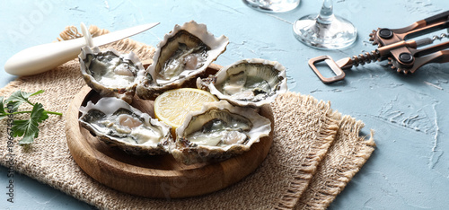 Foto Wooden plate with delicious fresh oysters, lemon and parsley on blue background,