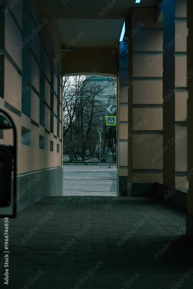 Fototapeta premium Framed Street View Through Archway Opening, Leafy Trees Visible Beyond, Pedestrian Sign Glowing Green, Textured Pavement And Wet Sheen, High Contrast